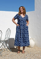 Woman posing in a relaxed fit, short sleeved, floral cotton dress with V- neckline, drawstring waist tie and pockets 