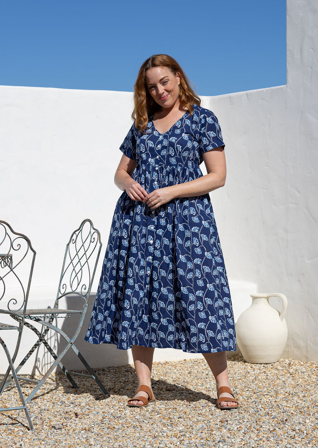 Woman wearing a relaxed fit, button through cotton dress in navy blue base floral print with V neckline.