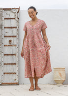 Woman posing in a relaxed fit, short sleeved, floral cotton dress with V- neckline, drawstring waist tie and pockets 