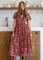 Woman standing in a 100% cotton floral print dress with a V-neckline, short sleeves, pockets, and buttons through to the knee.
