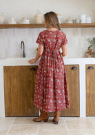 Woman stands backwards wearing a 100% cotton dress with short sleeves, pockets, and a drawstring tie at the back.