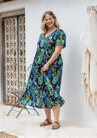 A woman wearing a short-sleeve V-neck button through cotton midi length dress with a colourful floral and peacock print.