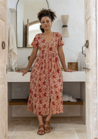 Woman wearing a relaxed fit, button through cotton dress in cream based floral print with V neckline.