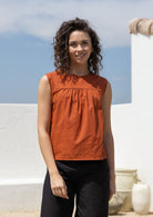 Woman wears rust tone cotton sleeveless top with small gathers across the bust