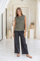 Woman wears olive green 100%  cotton sleeveless top with small gathers across the bust and high round neckline.