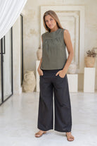 Woman wears cotton sleeveless top in olive green with gathers under the square neckline yoke.