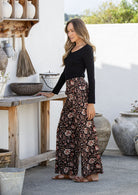woman stands sideways wearing a 100% cotton pant in black based floral print paired with a basic top