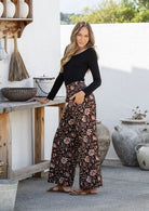 Woman wearing a black top and black floral pants standing outdoors.