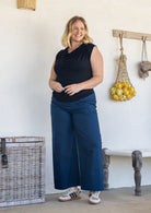 A woman  wearing a sleeveless black cowl-neck top and blue wide-leg cotton pants, paired with white sneakers.