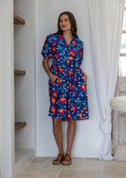 Woman wearing a knee length relaxed fit button through 100% cotton dress with elbow length sleeves and hand in pockets.