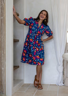 Woman wearing royal blue based floral print 100% cotton dress with, relaxed fit, empire waistline and elasticated elbow length sleeves