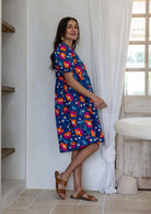 Woman standing sideways wearing a 100% cotton short sleeve dress in royal blue based floral print