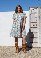 Woman wearing white based floral print 100% cotton dress with, relaxed fit, empire waistline and elasticated elbow length sleeves