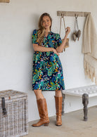 Woman stands wearing navy blue based floral print 100% cotton dress with elasticated elbow length sleeves