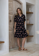 Woman wearing black based floral print 100% cotton dress with, relaxed fit, empire waistline and elasticated elbow length sleeves