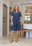 Woman wearing a knee length relaxed fit button through 100% cotton dress with one hand in pocket