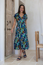 Woman standing backwards in blue based floral midi length rayon button through dress with V-neckline and elasticated waistband