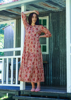 Woman poses floral cotton maxi dress with buttoned bodice, 3/4 sleeves and flowy three tiered maxi skirt