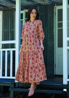 Woman poses in cream based floral cotton maxi dress with buttoned bodice, 3/4 sleeves and flowy three tiered maxi skirt