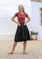 Woman wearing terracotta basic top and black cotton pleated skirt with button through front, pockets and belt loops.