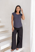 Woman wearing a 100% rayon dark grey top and black pants standing in a room with white walls and a staircase.
