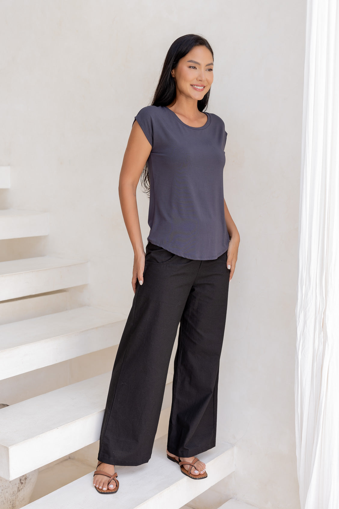 Woman wearing a 100% rayon dark grey shell t-shirt top and black pants standing on a white staircase.