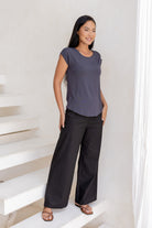 Woman wearing a 100% rayon dark grey shell t-shirt top and black pants standing on a white staircase.