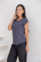 Woman with hand on face wearing a 100% rayon dark grey shell t-shirt and black pants against a white background