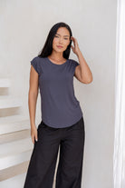 Woman wearing a 100% rayon grey shell t-shirt and black cotton pants against a white wall.
