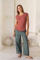 Woman wearing a 100% rayon terracotta shell t-shirt with plain green pants in an indoor setting