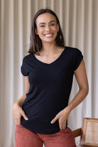 Woman wearing a black stretch rayon jersey t-shirt with a V-neck and cap sleeves, with hands in pants pockets