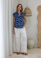Woman standing wearing a 100% cotton blue based floral top paired with a plain white pants