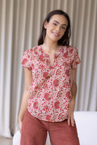 Woman wearing a 100% cotton gentle cream based floral blouse and plain pants standing against a white wall.