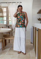 Woman standing wearing white cotton pants paired with sleeveless floral cotton top with high round neckline