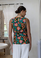 Woman standing backwards wears 100% cotton floral top, sleeveless design. 