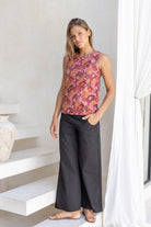 Woman standing in sun wearing black cotton pants paired with sleeveless floral cotton top with high round neckline