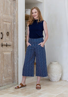 Model standing wearing a 100% cotton capri style wide leg pants in navy based white striped print and side pockets