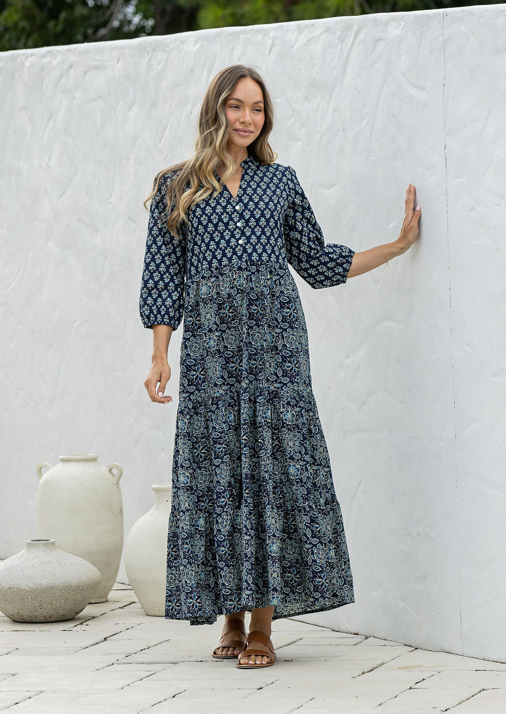 Woman standing in navy blue based 100% cotton flowy tiered maxi dress with 3/4 sleeves, buttoned bodice and pockets 