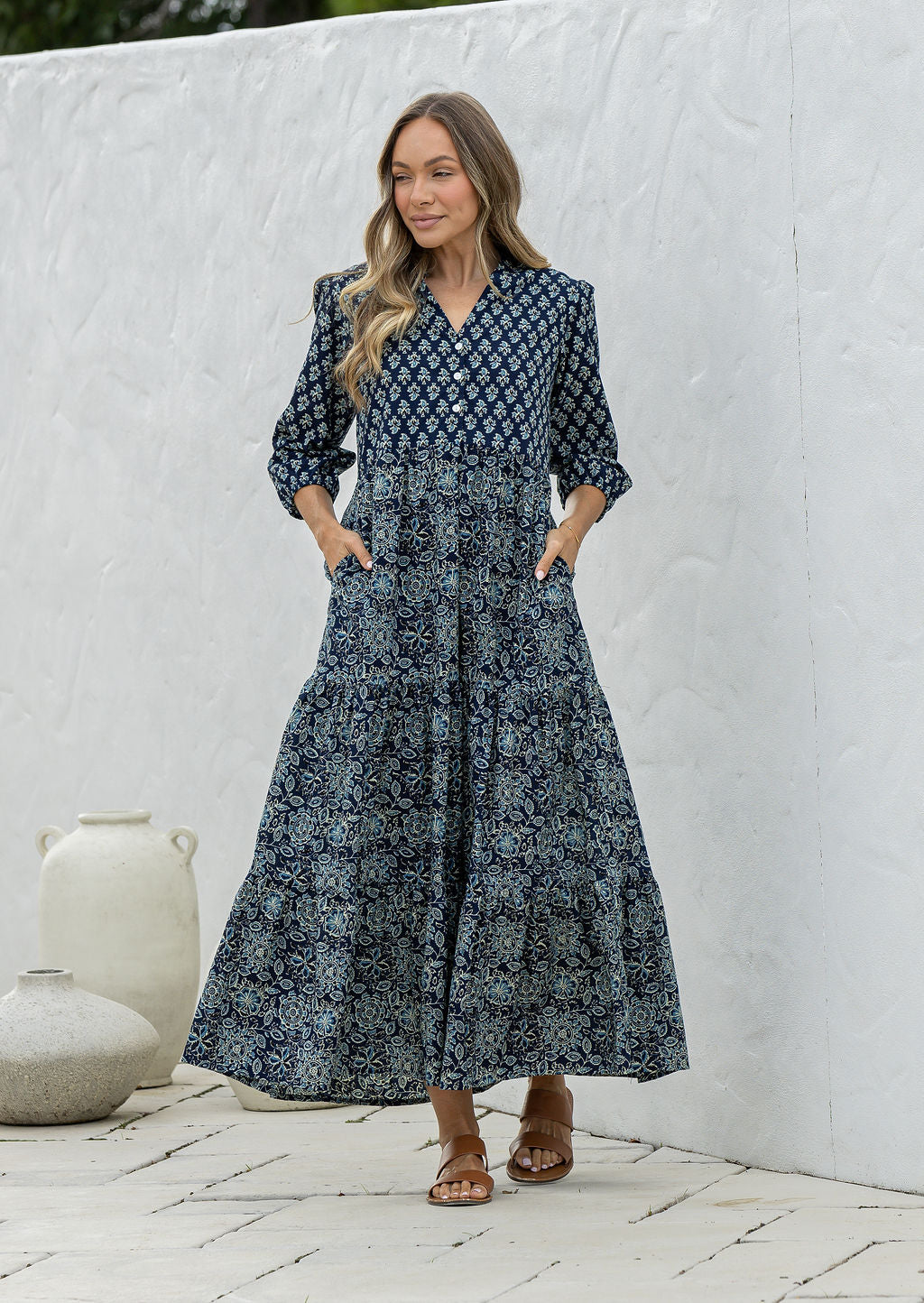 Woman poses in navy blue based floral cotton maxi dress with buttoned bodice, 3/4 sleeves and flowy three tiered maxi skirt