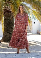 Woman standing in red based 100% cotton flowy tiered maxi dress with 3/4 sleeves, buttoned bodice and pockets 