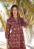Woman in a red floral dress standing under a palm tree