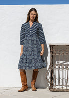 Woman wearing a 100% cotton tiered over the knee dress with 3/4 sleeves, buttoned bodice and V-neckline