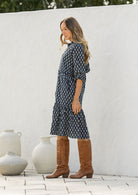 Model stands side on in cotton over the knee length relaxed fit dress with 3/4 sleeves, paired with tan sandals 