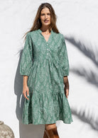 Woman poses in cotton tiered over the knee dress with 3/4 sleeves, buttoned bodice and V-neckline
