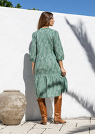 Model stands backwards in cotton over the knee length relaxed fit dress with 3/4 sleeves, paired with brown boots. 