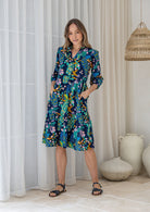 Woman poses in cotton tiered over the knee dress with 3/4 sleeves, buttoned bodice and V-neckline