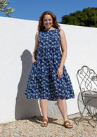 Woman wears a sleeveless, relaxed fit  floral cotton dress with tiered style, empire waist and pockets.
