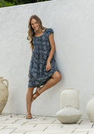 Woman wearing a 100% cotton navy blue based floral dress with round neckline and cap sleeves.