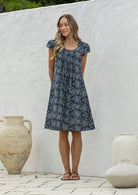 Woman standing wearing a 100% cotton navy blue based floral dress with round neckline.