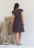 Woman stands backwards wearing a 100% cotton black based floral dress with round neckline.
